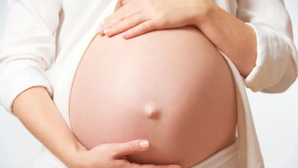 Femme enceinte entourant son ventre de ses bras