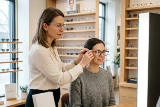 Opticienne visagiste tenant une monture devant le visage d'une cliente dans une boutique d'optique moderne