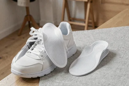 Semelles orthopédiques Akusoli insérées dans une chaussure blanche posée sur parquet, vue de dessus montrant le soutien de la voûte plantaire
